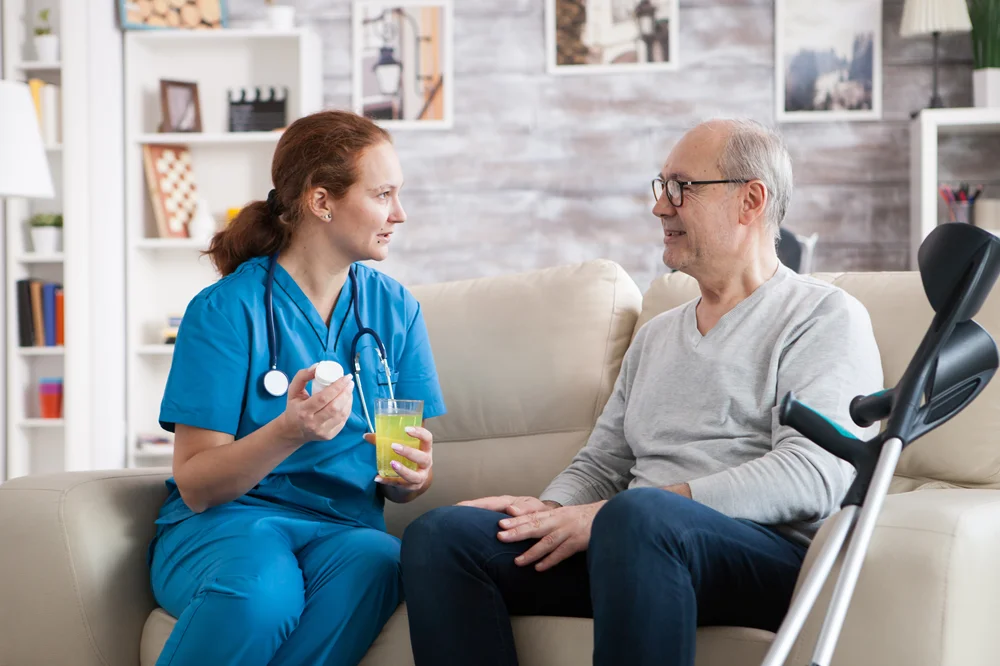 Caregiver giving tea to an elderly patient at home